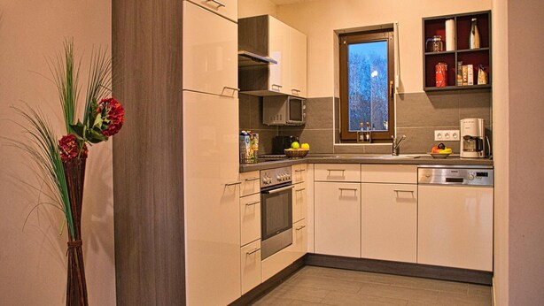 Une cuisine moderne avec des meubles blancs, un four à micro-ondes, une cuisinière et une fenêtre donnant sur les arbres.