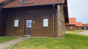 Un bâtiment en bois avec une porte marron, deux fenêtres avec volets et un toit recouvert de tuiles rouges.