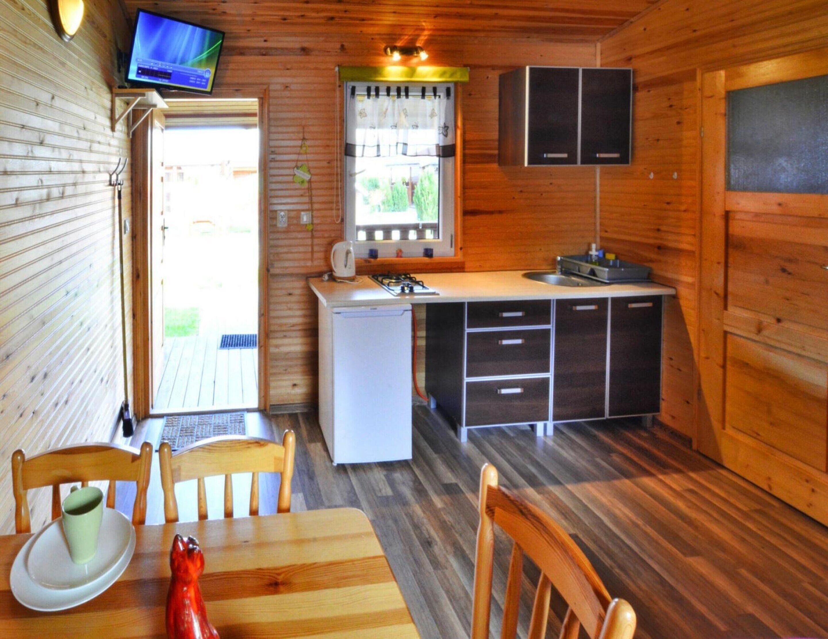 A compact kitchen with a refrigerator, stove, sink, and cabinets. There is a dining table with chairs and a television mounted on the wall.
