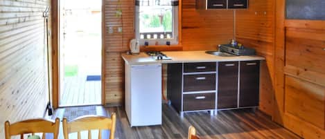 A compact kitchen with a refrigerator, stove, sink, and cabinets. There is a dining table with chairs and a television mounted on the wall.