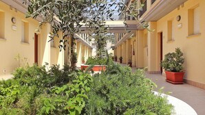 A narrow, covered pedestrian walkway flanked by buildings with balconies and potted plants. - Apartment in Villassimius Garden (Villasimius)