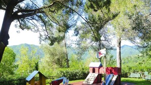 Un terrain de jeux avec des toboggans et des structures d’escalade, entouré d’arbres et offrant une vue sur la montagne.