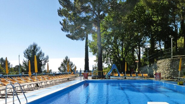 Une piscine avec un toboggan, entourée de chaises longues et de grands arbres.