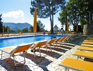 A poolside area with lounge chairs and a swimming pool, surrounded by trees and mountains in the background. - Holiday Resort in Villanova D'albenga (Villanova d'Albenga)