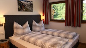 Una camera da letto con un letto, due cuscini, un comodino, una lampada, una finestra con tende e un quadro appeso al muro.