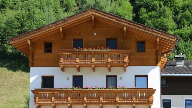 Un edificio a più piani con facciata in legno, balconi fioriti e una sezione inferiore bianca.
