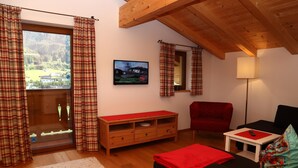 Un accogliente soggiorno con una panca di legno, una poltrona rossa, un divano nero e un tavolino con un telecomando.