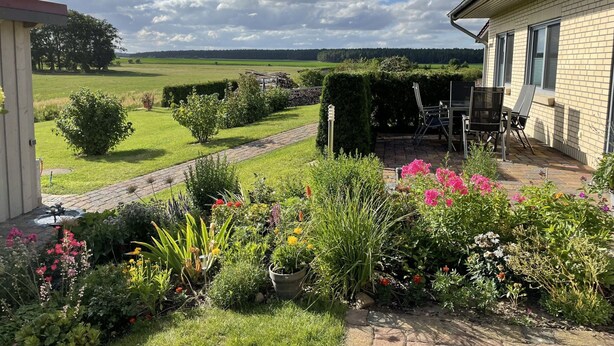 Un jardin agrémenté d’une terrasse, d’un chemin en briques et offrant une vue sur un champ et des arbres au loin.