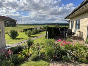 A garden with a patio area, a brick pathway, and a view of a field and trees in the distance. - Ferienhaus Wiesenblick in Dobbertin (Dobbertin)