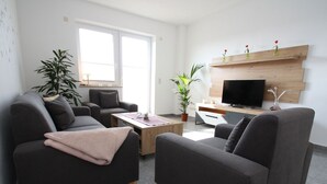 Un salon moderne avec deux canapés, une table basse, un téléviseur et une étagère en bois ornée de vases.
