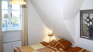 A bedroom with a bed, a window with curtains, a lamp, and a painting on the wall. - Ferienwohnung in Oevenum auf Foehr (Oevenum)