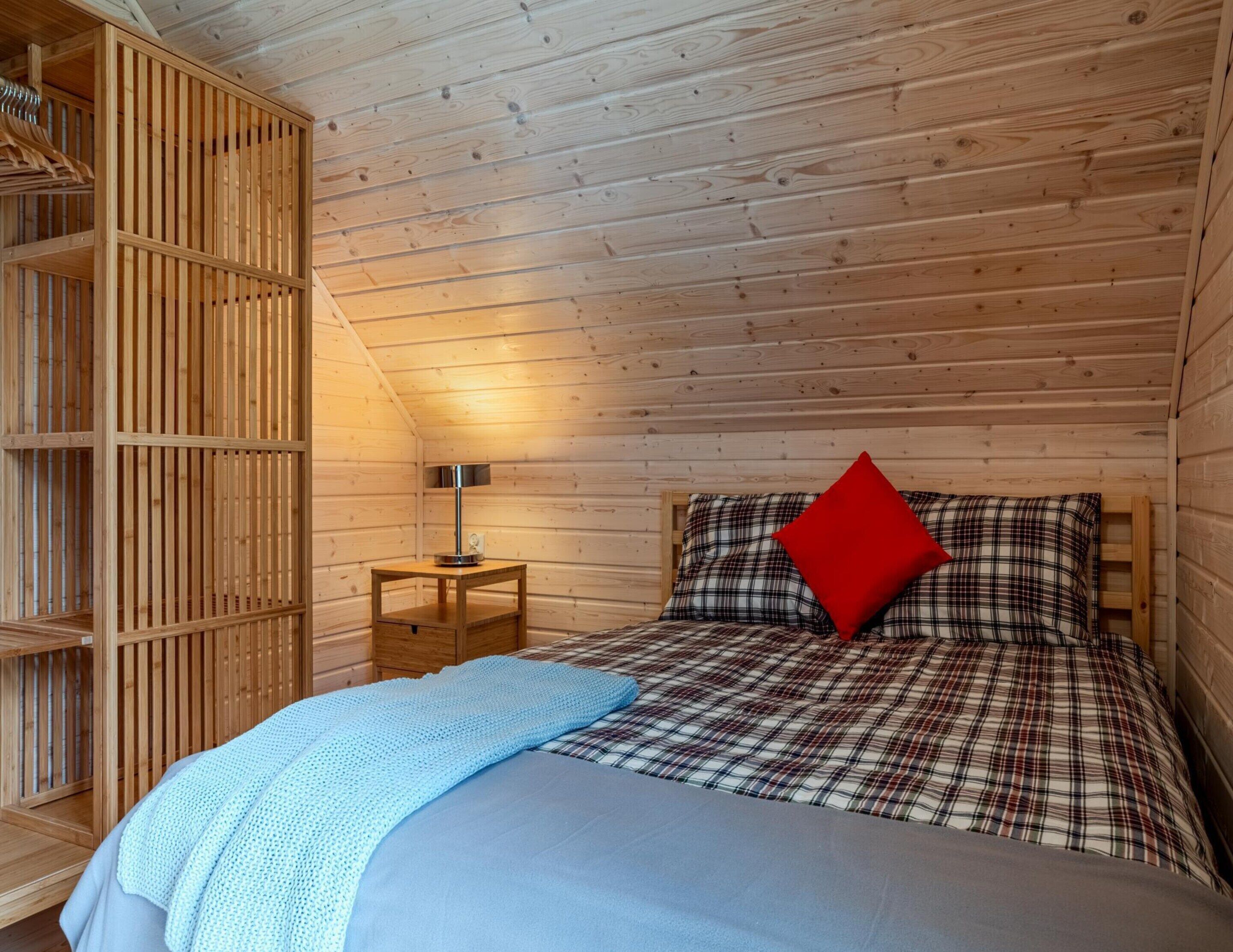 A cozy bedroom with a bed, a nightstand, a lamp, and a wardrobe.