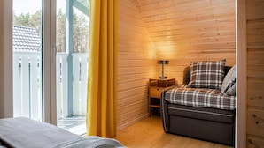 Ein gemütliches Cabin-Zimmer mit Bett, Sofa, Lampe und einem Fenster mit gelben Vorhängen.