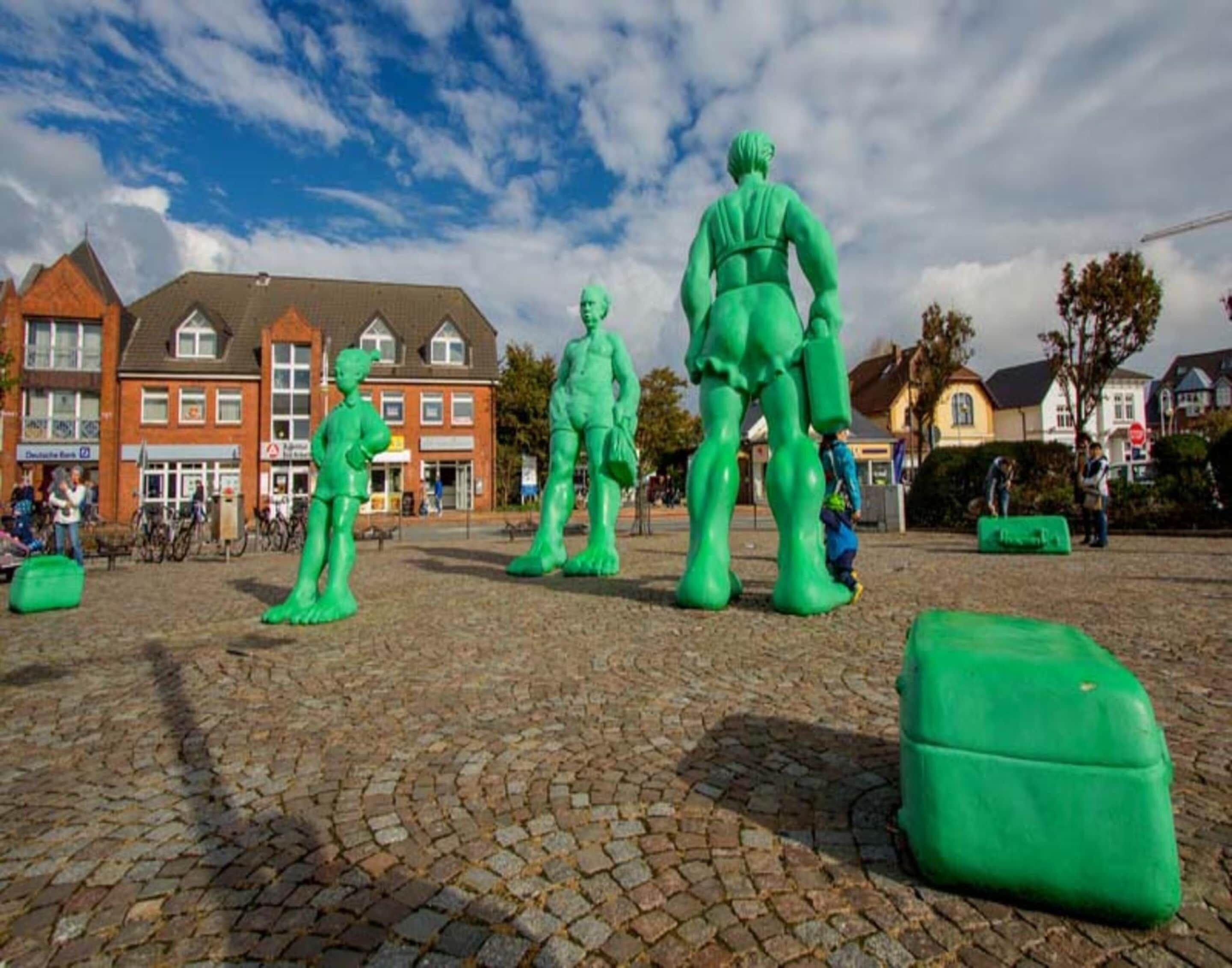 A cobblestone plaza with green sculptures and a row of brick buildings in the background.