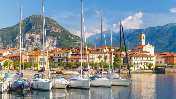 A marina with several sailboats docked, a mountain in the background, and buildings with red roofs. - Timeless l Antico Mulino Della Bozza (Brebbia)