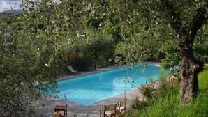 A swimming pool surrounded by lush greenery, with a small table and chairs nearby. - App. Agriturismo Monteverde, Castelnuovo Magra (Castelnuovo Magra)