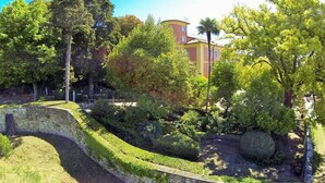 A landscaped garden with a curved stone wall, various trees, and a building in the background. - App. Agriturismo Monteverde, Castelnuovo Magra (Castelnuovo Magra)