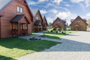 A row of log cabins with a cobblestone driveway and a well-maintained lawn. - Comfortable Houses With Swimming Pools, Rewal (Rewal)