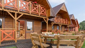 Eine Holzhütte mit einer Terrasse, Sitzgelegenheiten im Freien und einem großen Fenster.