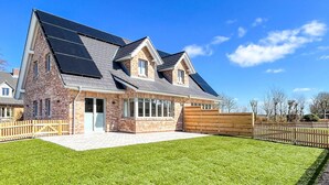 A modern two-story house with a sloped roof, solar panels, and a well-maintained lawn. - Moderne Doppelhaushalfte in Niebull (Niebuell)
