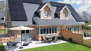 A modern house with a sloped roof, solar panels, a brick exterior, and a patio with outdoor furniture. - Moderne Doppelhaushalfte in Niebull (Niebuell)