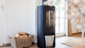 Un intérieur moderne avec un poêle à bois noir, un panier en osier rempli de bois de chauffage et une porte vitrée donnant sur l’extérieur.