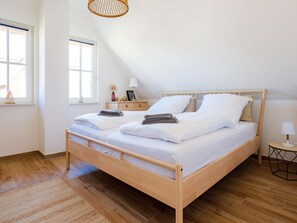 A double bed with white linens, a bedside table with a lamp, and a small nightstand with a vase and picture frame. - Ferienhaus mit Sauna in Boiensdorf (Boiensdorf)