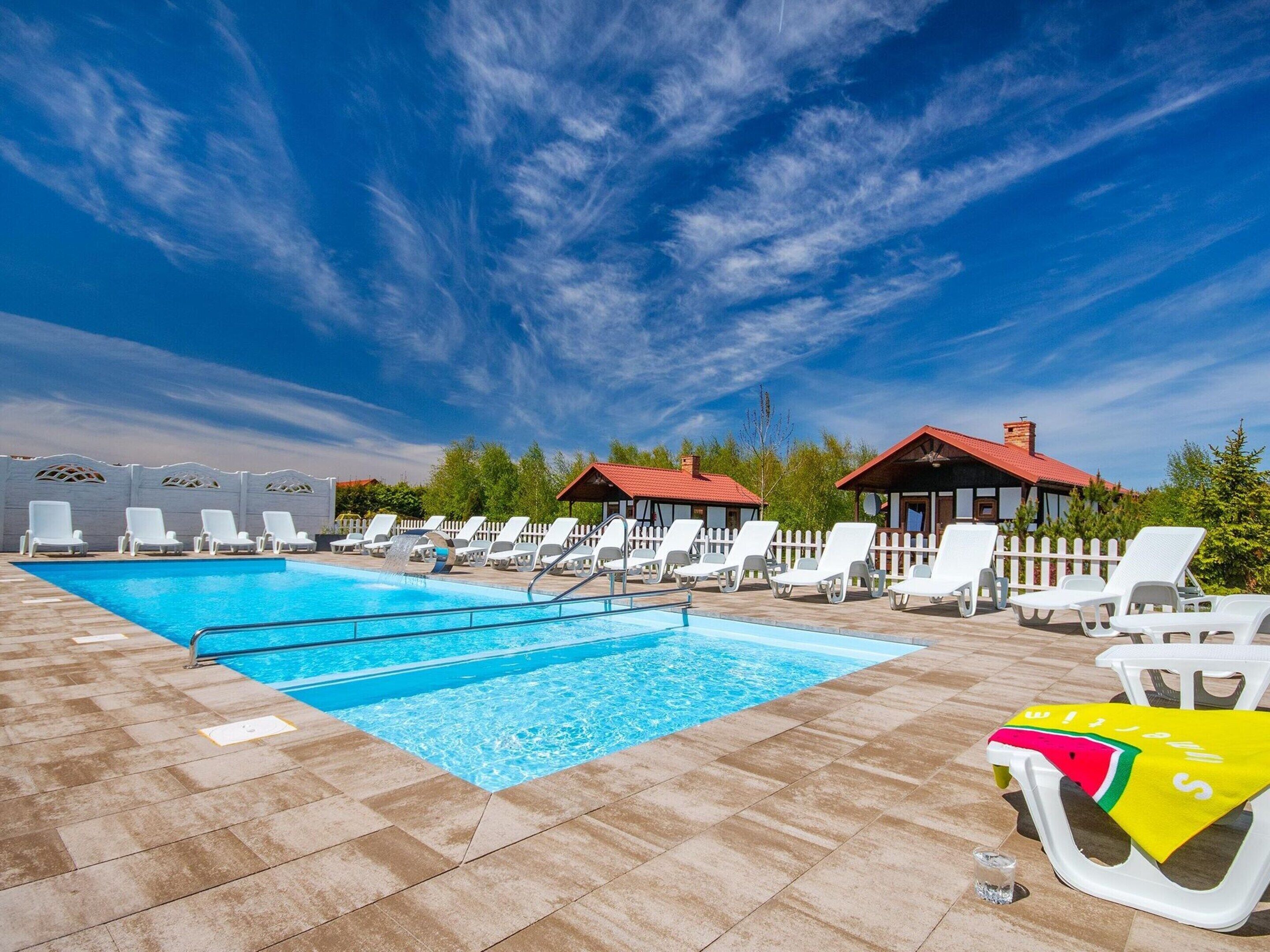 A swimming pool area with lounge chairs and a small building with a red roof.
