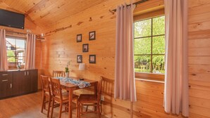 Ein Holzblockhaus-Innenraum mit Esstisch, Stühlen, einem kleinen Schrank und einem Fenster mit Vorhängen.
