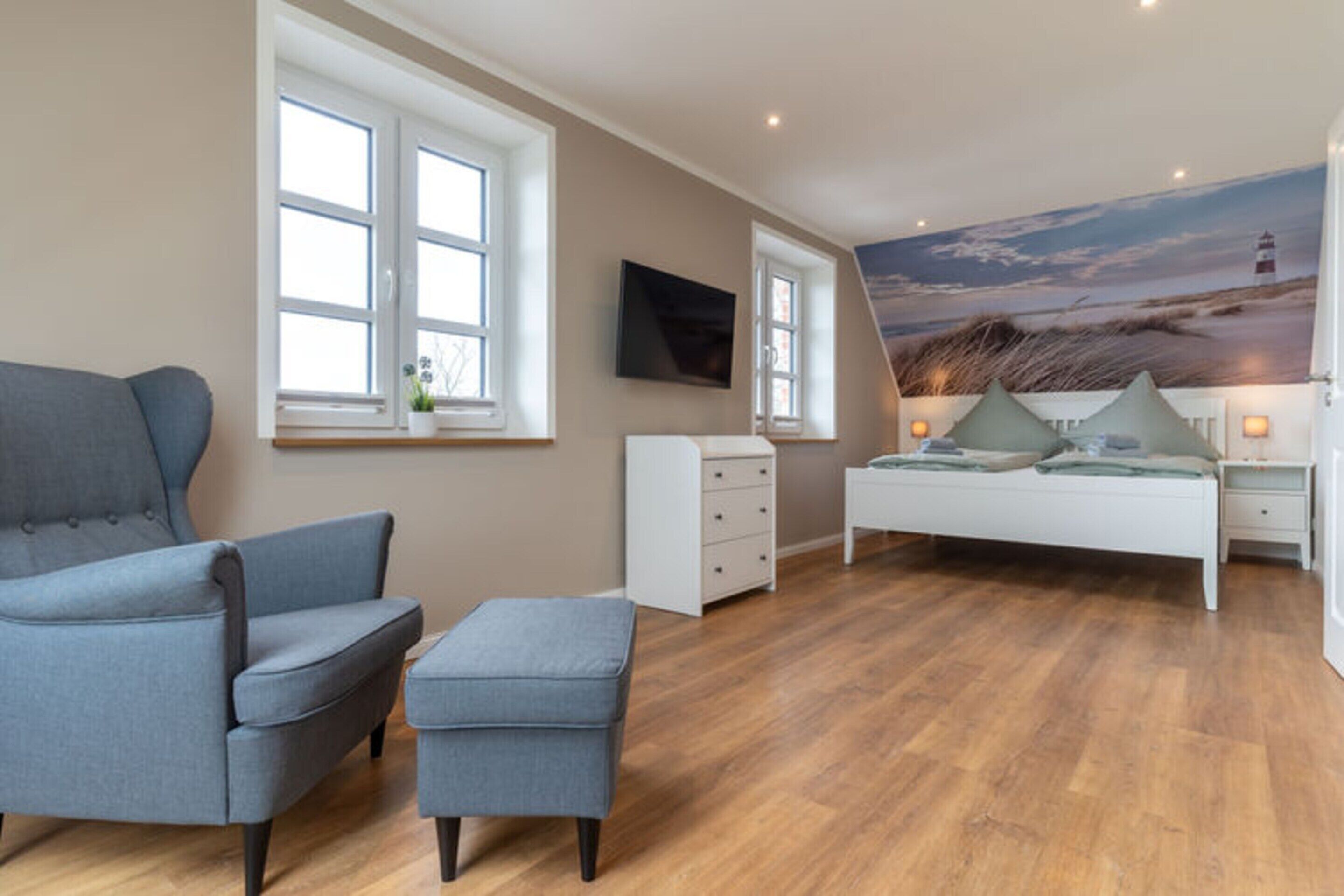 A bedroom with a bed, a chair, a small table, and a TV.