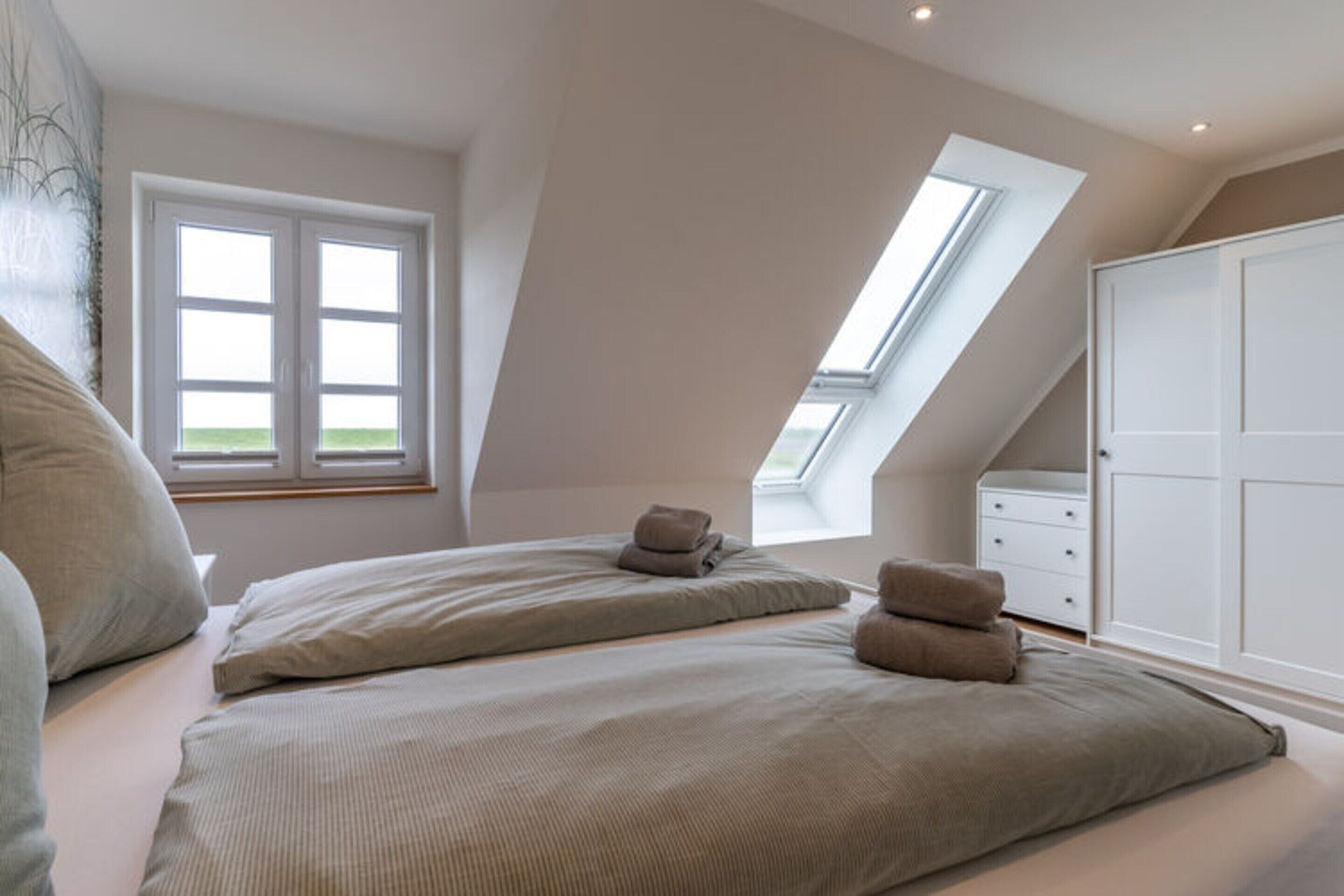 A bedroom with a sloped ceiling, a skylight, a bed with pillows, a nightstand, and a wardrobe.