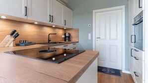 A modern kitchen with a wooden countertop, built-in cabinets, a stove, and a coffee maker. - Doppelhaushalfte in Karolinenkoog (Karolinenkoog)