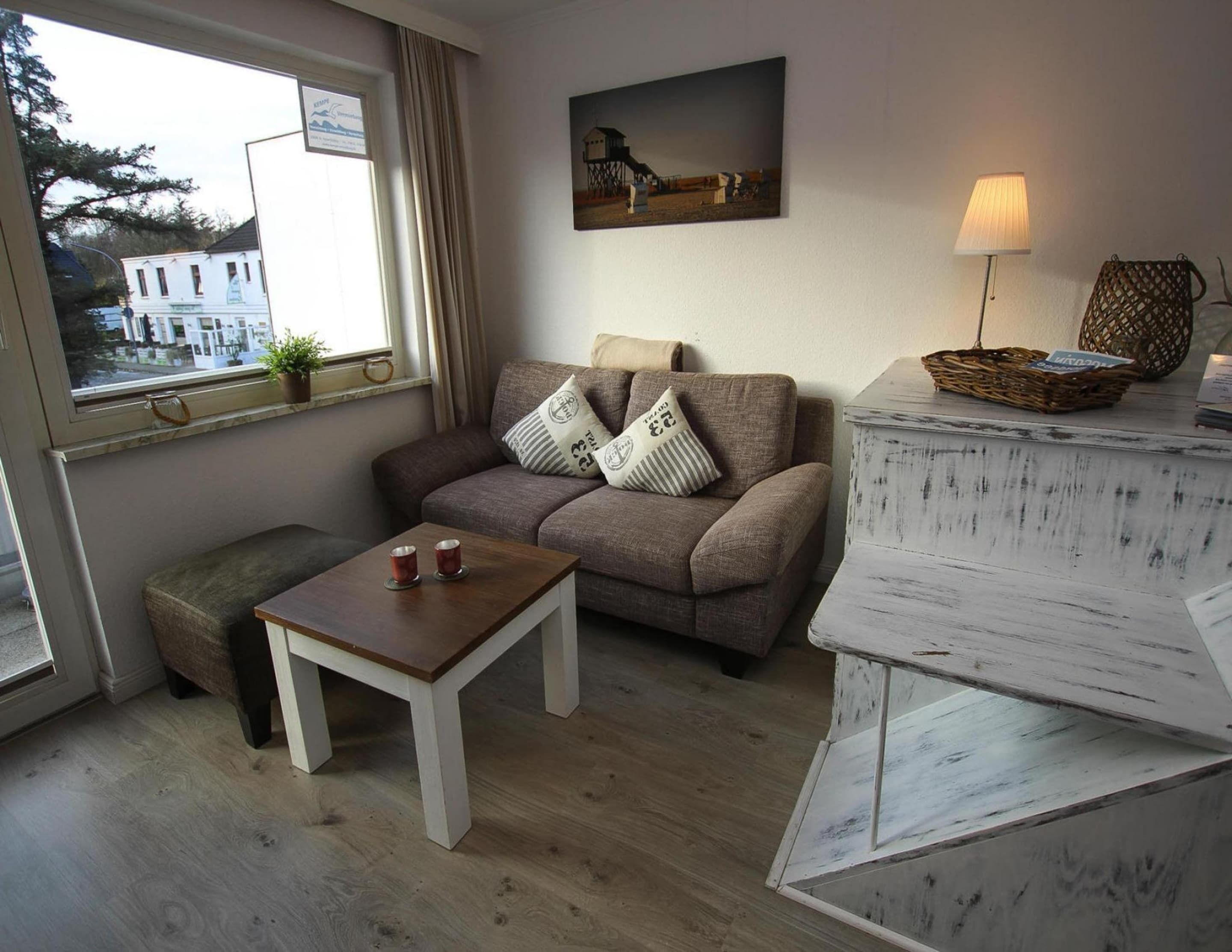 Un salon confortable avec un canapé, une petite table et une lampe. Une fenêtre offre une vue sur un bâtiment situé à l’extérieur.