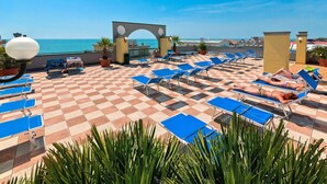 A rooftop terrace with checkered flooring, blue lounge chairs, and a view of the sea. - Residence Cristoforo Colombe Caorle (Caorle)