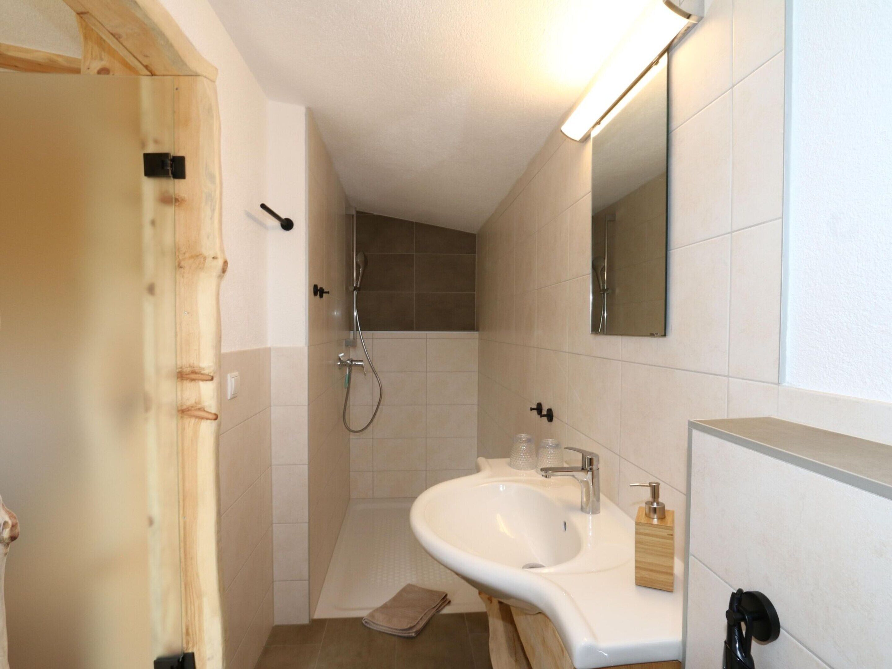 A bathroom with a wooden door, a white sink, a mirror, and a shower.