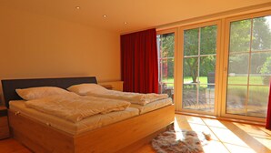Une chambre dotée d’un grand lit, d’une tête de lit en bois et d’une porte-fenêtre coulissante donnant sur une terrasse.