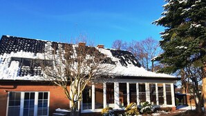 Une maison dont le toit est recouvert de neige, avec de grandes fenêtres et une façade en briques.