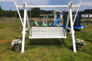 A white swing set with a bench, surrounded by a grassy field and a fence.