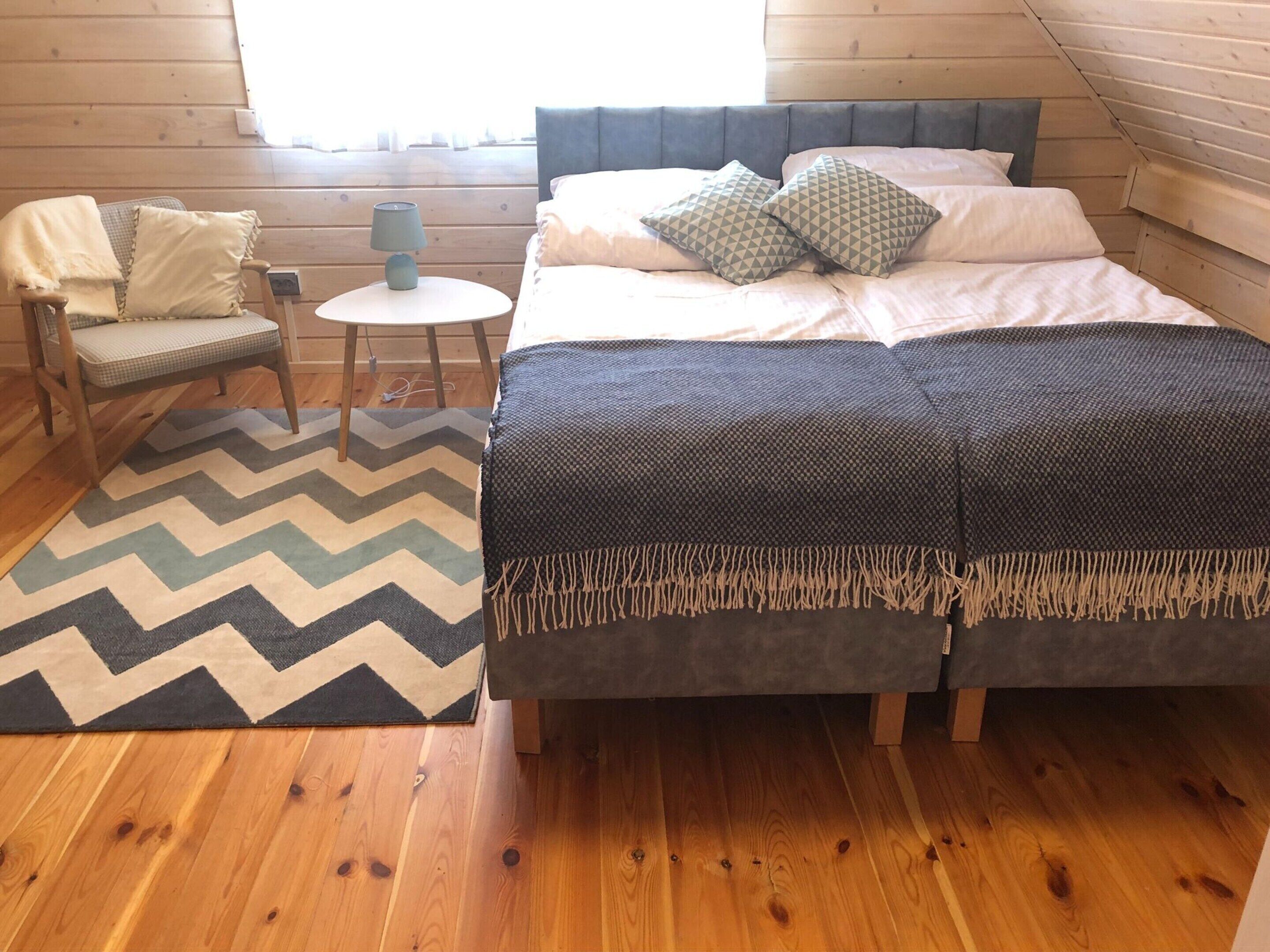 Une chambre confortable avec un lit, une chaise, une petite table et un tapis à motifs chevrons.
