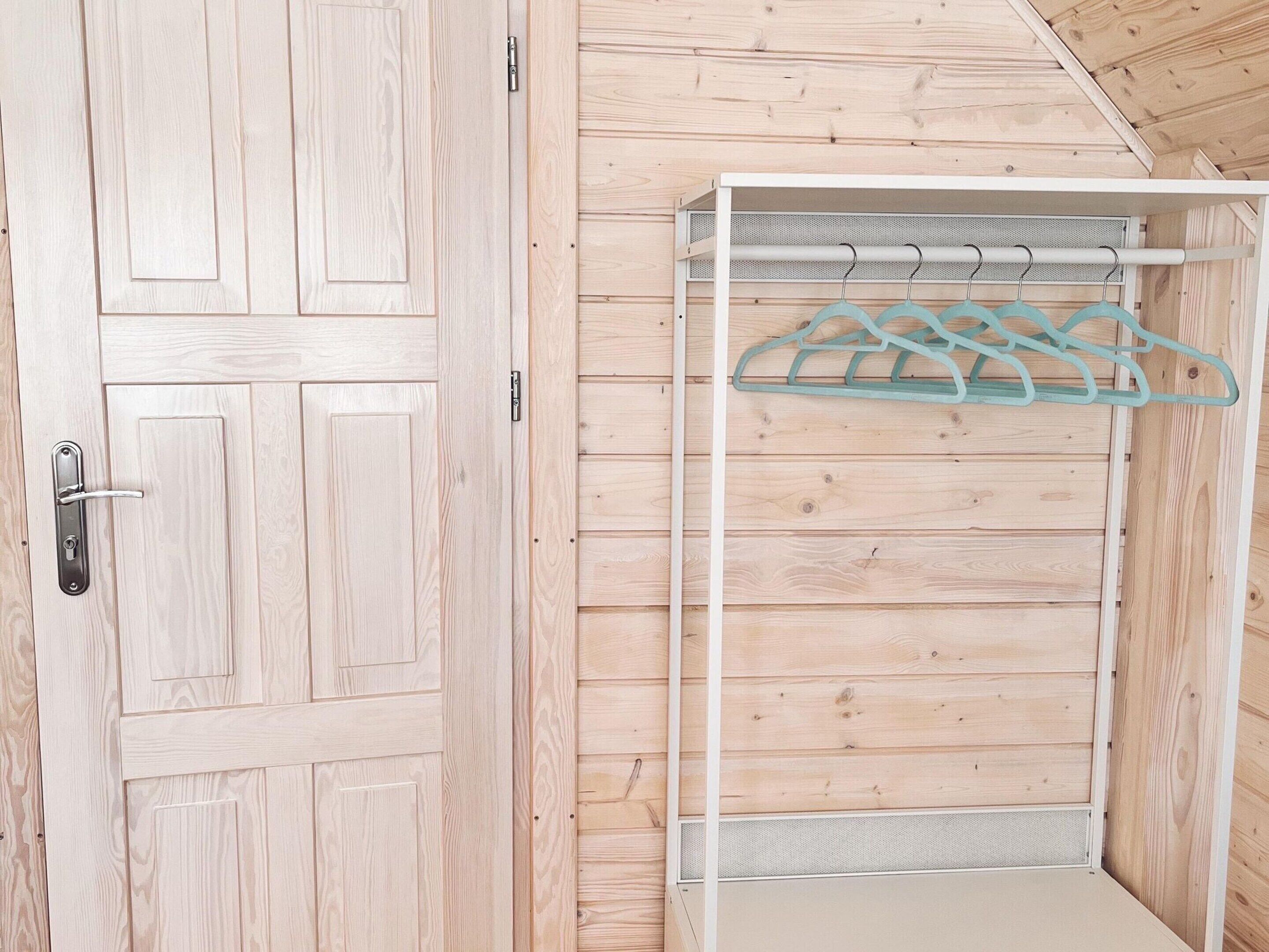 A wooden room with a white wardrobe and a metal rack with clothes hangers.