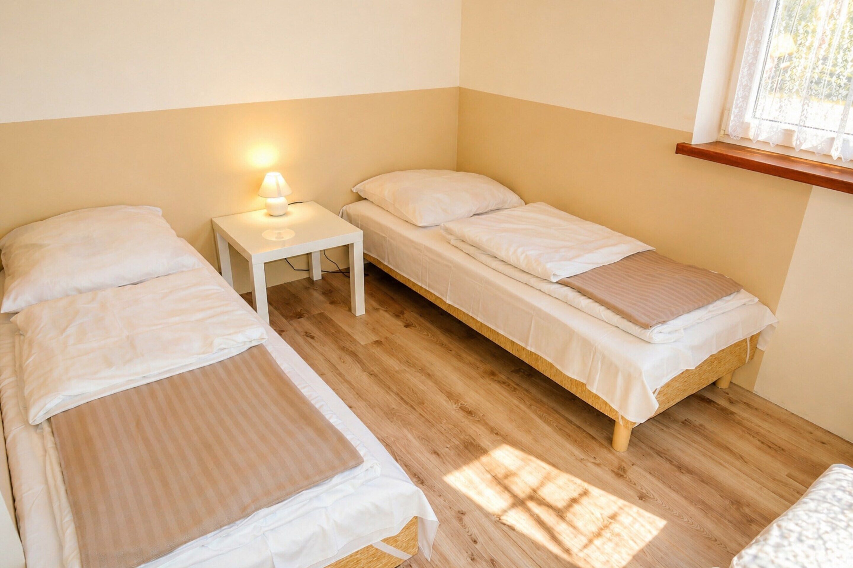 Une chambre avec deux lits simples, une table de chevet avec une lampe et une fenêtre donnant sur un beau paysage.