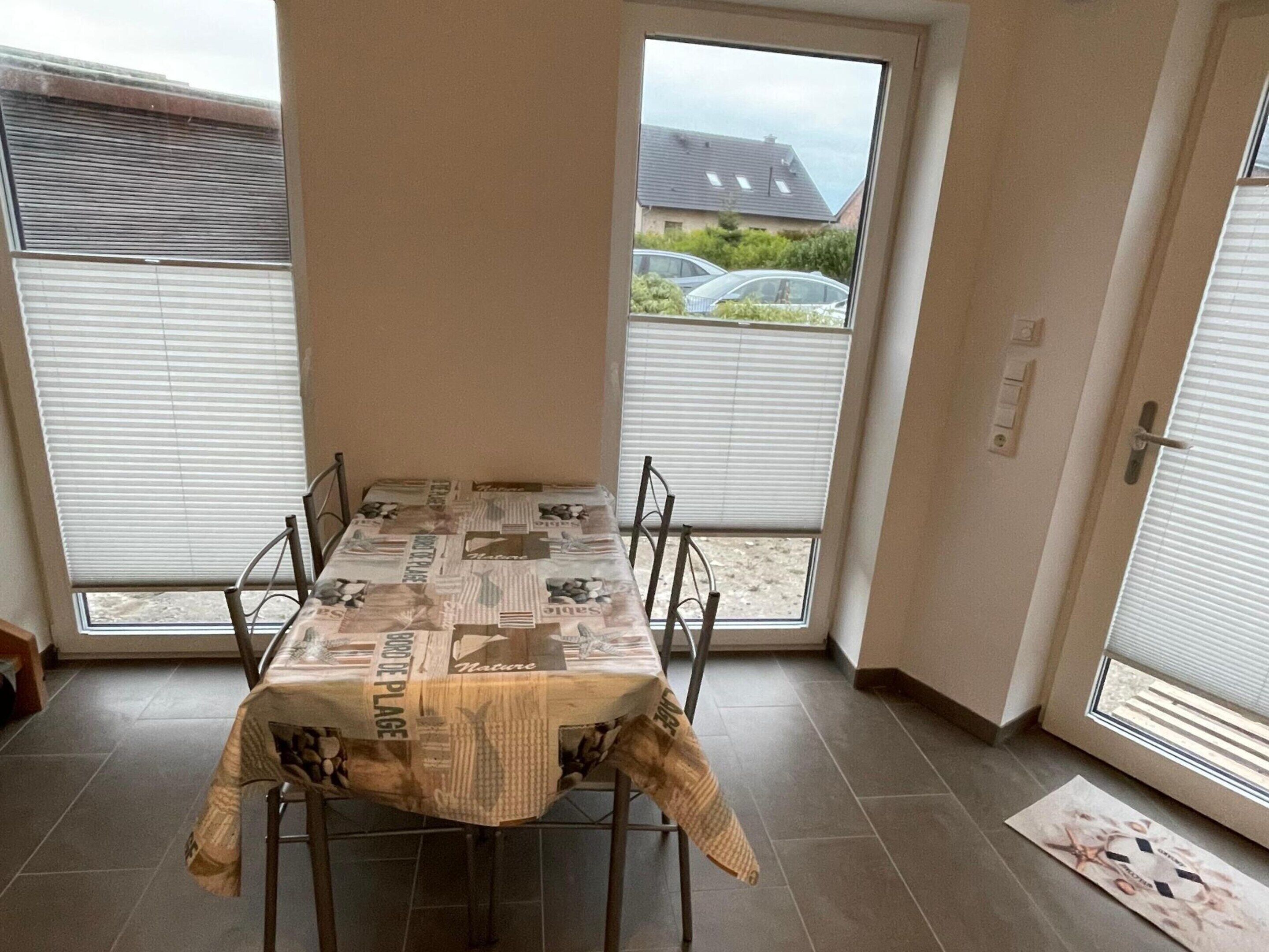 A dining area with a table covered in newspaper, four chairs, and large windows with blinds.