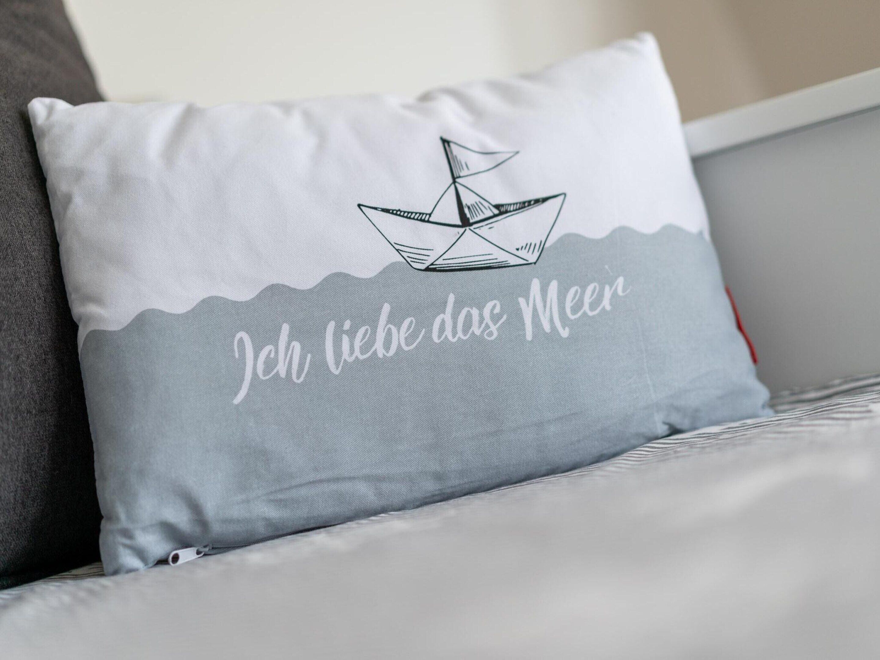 A pillow with a boat and text on a bed.
