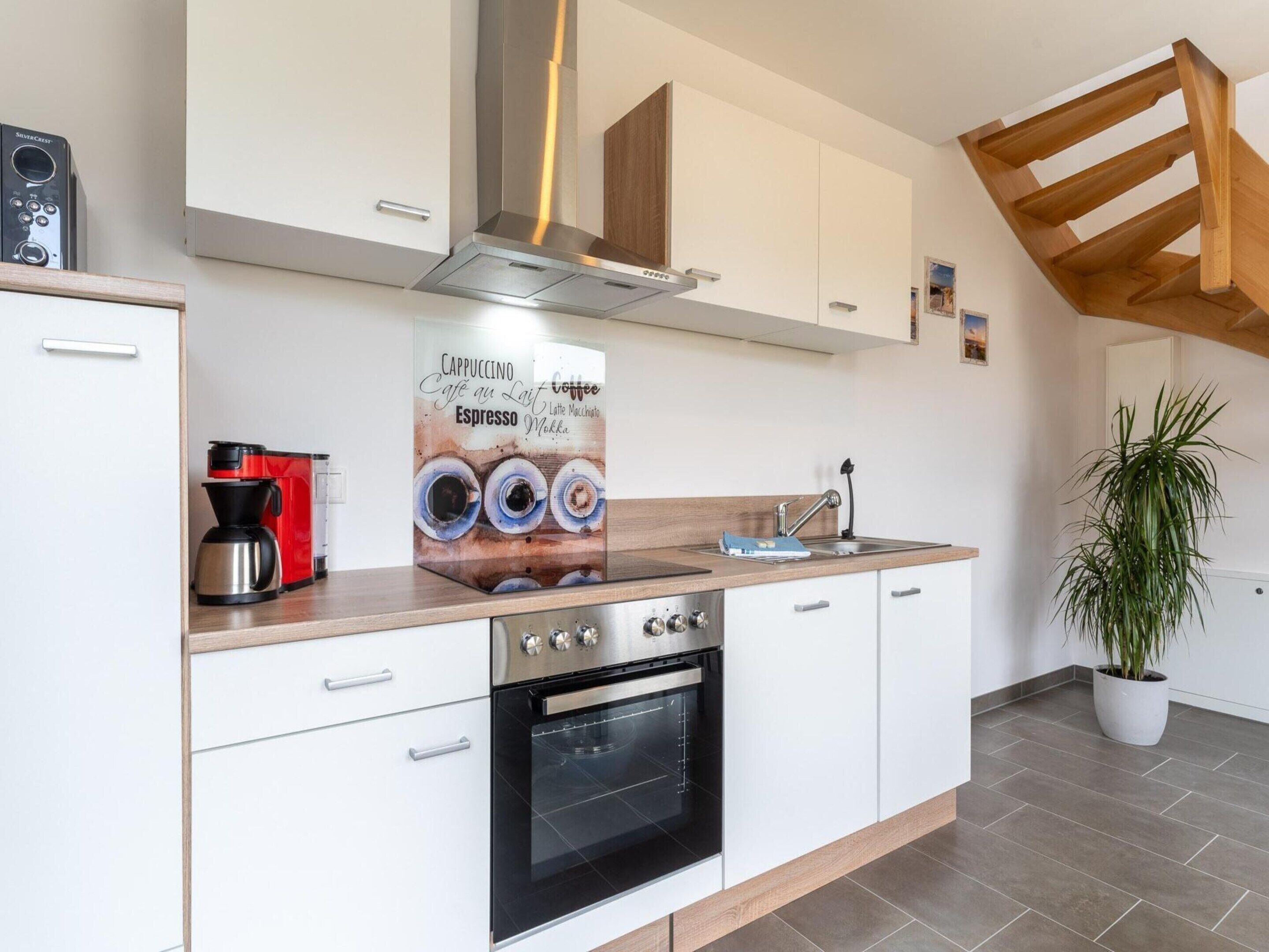 A modern kitchen with white cabinetry, a built-in oven, a coffee machine, and a large poster of coffee cups.