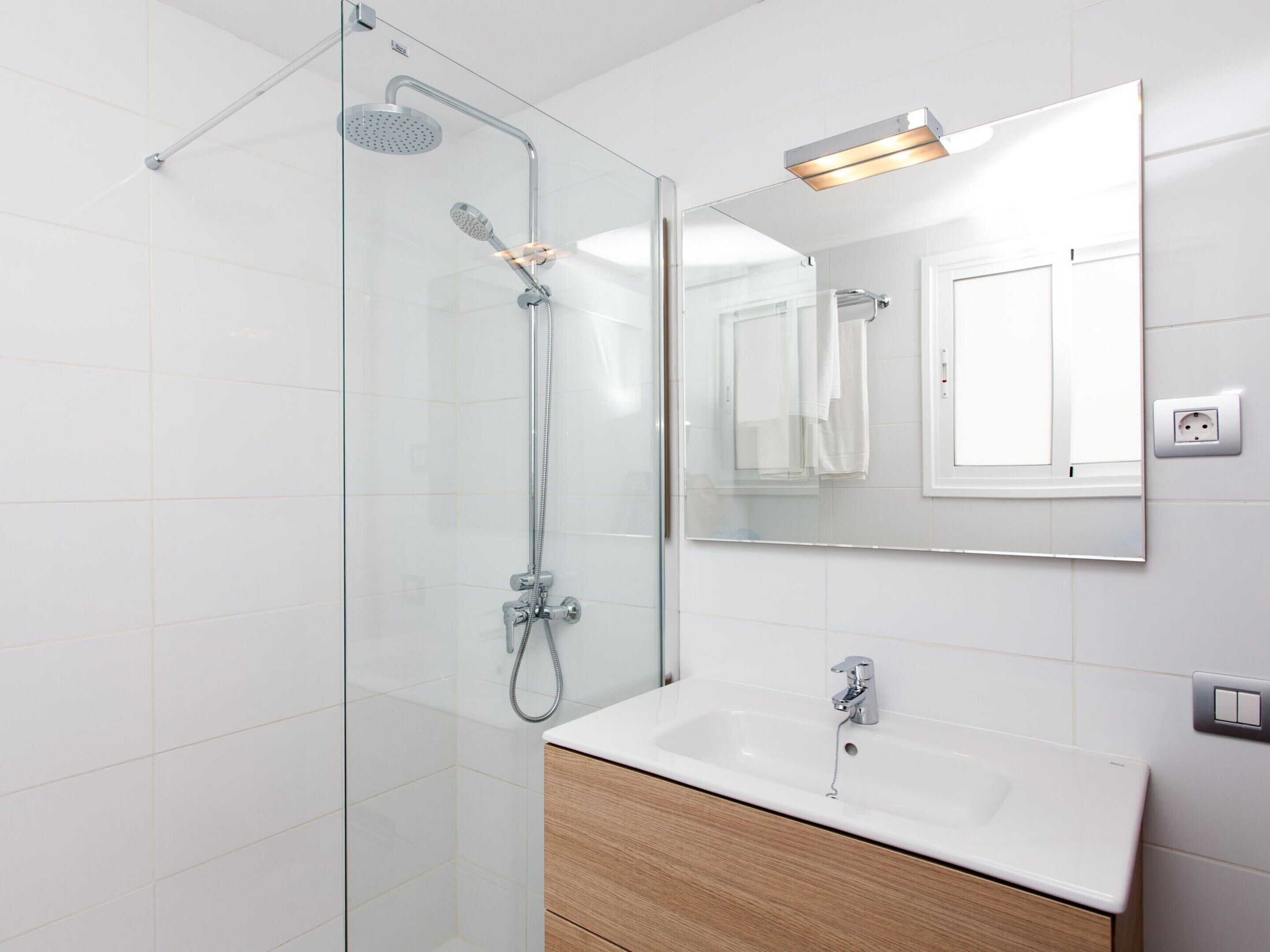 A modern bathroom with a glass shower enclosure, a white sink, and a mirror above it.