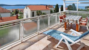 A balcony with a table and chairs, overlooking a body of water and buildings. - Apartment in Biograd Near Drazica Beach (Biograd na Moru)