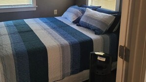 A bedroom with a bed, two windows with blinds, a door, and a ceiling light.