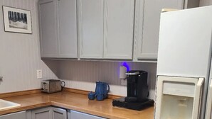 A kitchen with light grey cabinets, a wooden countertop, a toaster, a coffee maker, and a refrigerator.