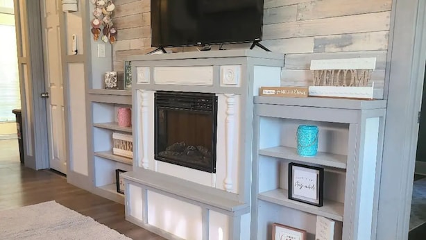 A living room with a fireplace, TV, and shelves with various decorations.