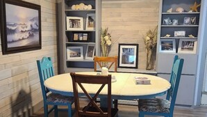 A dining area with a round table and four chairs, surrounded by wooden walls and shelves with framed pictures.